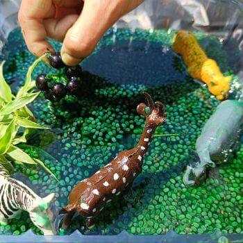 green and blue water with small green rock mixed in. Safari animal figurines in water to create a sensory bin.