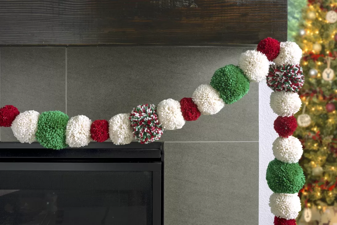Garland made out of red, white, and red yarn Pom poms and strung across a fireplace mantel